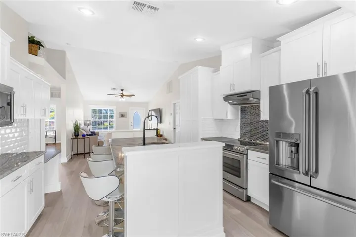 Kitchen with appliances with stainless steel finishes, backsplash, white cabinetry, and lofted ceiling