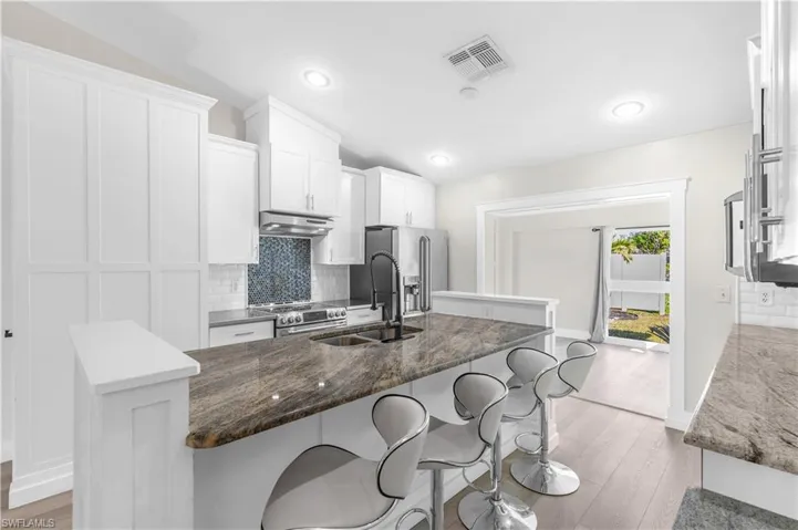 Kitchen with lofted ceiling, sink, an island with sink, appliances with stainless steel finishes, and white cabinetry