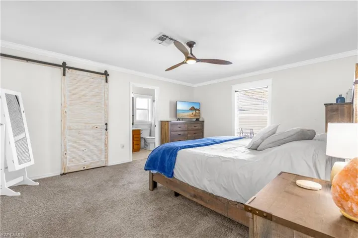 Bedroom with light carpet, ensuite bath, ceiling fan, a barn door, and ornamental molding