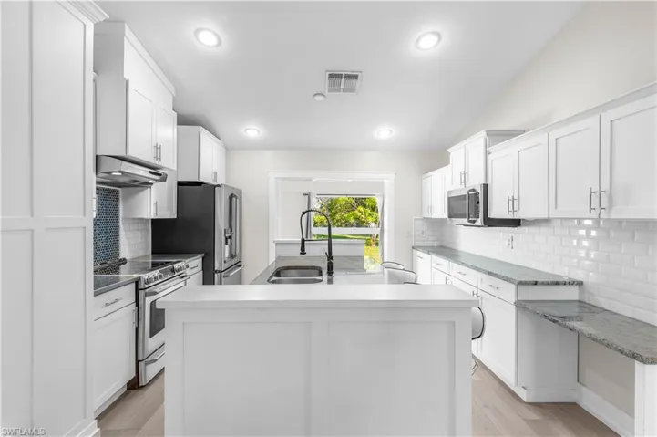 Kitchen with a kitchen island with sink, sink, white cabinets, and appliances with stainless steel finishes