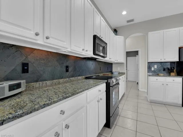 Kitchen with stainless steel appliances, white cabinets, light tile patterned flooring, dark stone countertops, and decorative backsplash