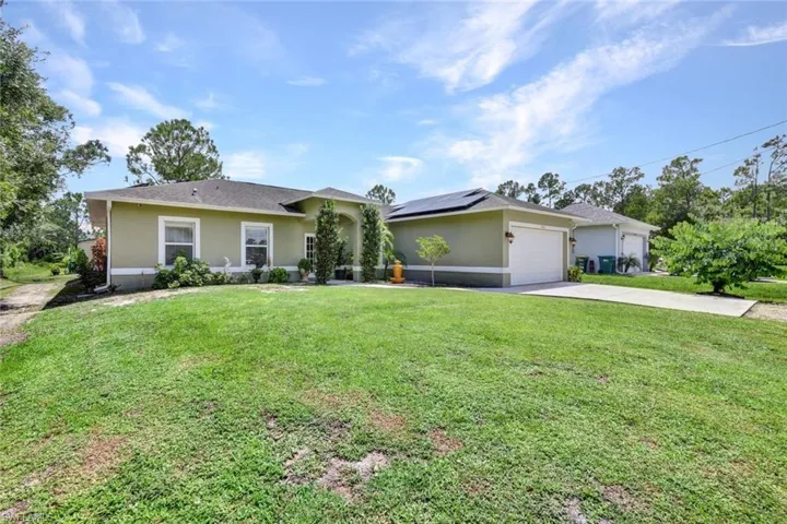 Ranch-style home featuring a garage, solar panels, and a front yard
