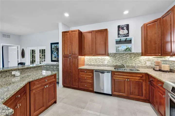 Kitchen with decorative backsplash, light stone countertops, sink, and stainless steel dishwasher