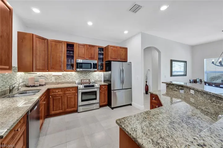Kitchen featuring light tile patterned floors, light stone counters, appliances with stainless steel finishes, decorative backsplash, and sink