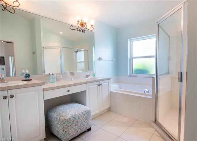 Bathroom with dual sinks, tile flooring, separate shower and tub, a notable chandelier, and large vanity