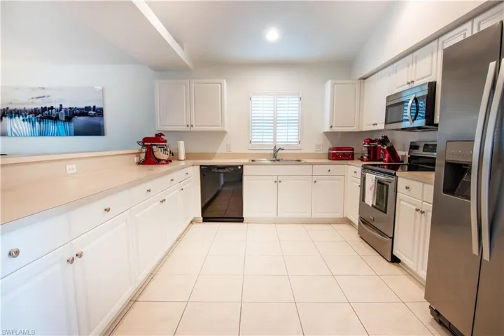 Kitchen with stainless steel appliances, white cabinets, sink, and light tile floors