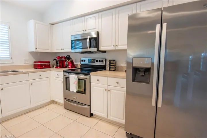Kitchen featuring sink, light tile flooring, white cabinetry, and appliances with stainless steel finishes