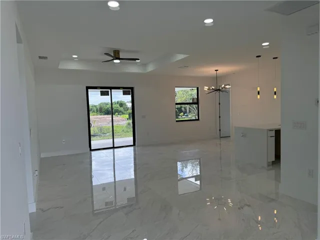 Spare room with a raised ceiling, ceiling fan with notable chandelier, and light tile floors