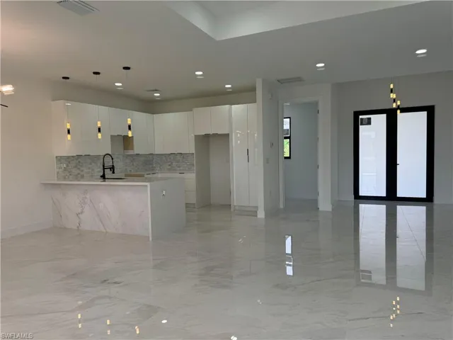 Kitchen with tasteful backsplash, pendant lighting, light tile floors, sink, and white cabinets