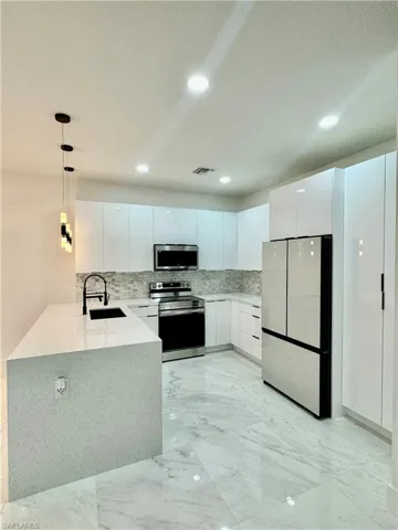 Kitchen with kitchen peninsula, tasteful backsplash, white cabinetry, and appliances with stainless steel finishes