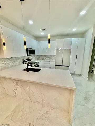 Kitchen with stainless steel appliances, kitchen peninsula, backsplash, pendant lighting, and light tile flooring