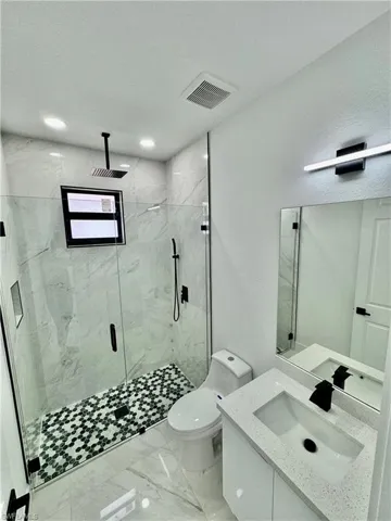 Bathroom featuring a textured ceiling, tile floors, a shower with shower door, toilet, and oversized vanity