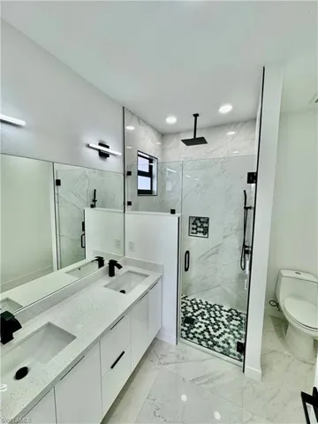 Bathroom with dual sinks, tile flooring, a shower with door, toilet, and large vanity