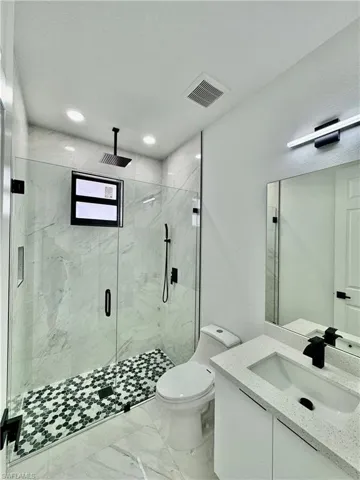 Bathroom with tile floors, an enclosed shower, toilet, and vanity
