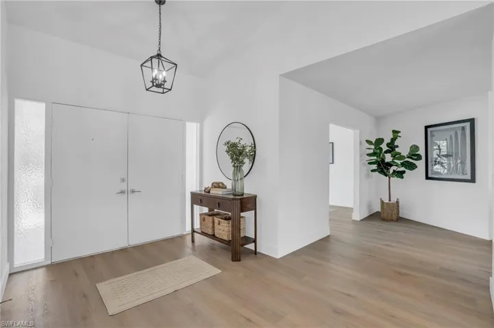 Entrance foyer with a notable chandelier, light wood-type flooring, and vaulted ceiling