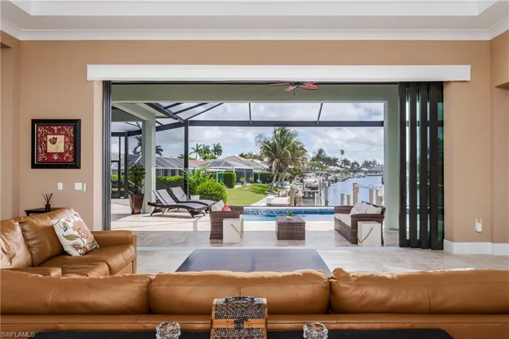 Expansive folding glass doors open to a screened lanai with a swimming pool, extending to a waterfront canal