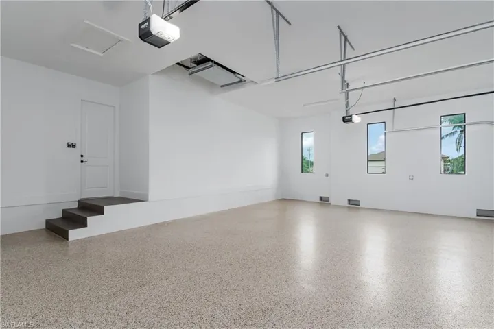 Spacious garage featuring a durable epoxy-coated floor, multiple windows providing natural light, and an interior access door with three steps