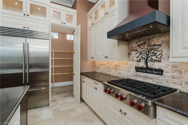 Gourmet kitchen featuring a stainless steel gas range, coordinating range hood, and a full-height brick-patterned backsplash