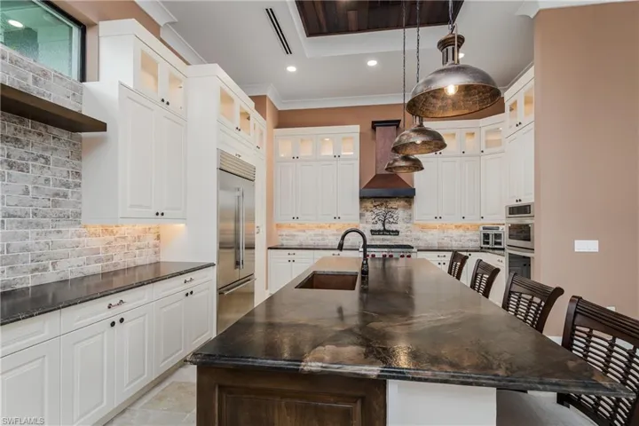 Gourmet kitchen featuring a large central island with seating, white shaker cabinetry, stainless steel appliances, a copper sink, and a brick-patterned backsplash