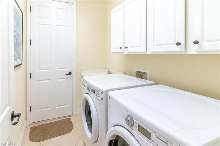 Laundry room featuring washing machine and clothes dryer, a sink, light tile patterned floors, cabinet space, and baseboards