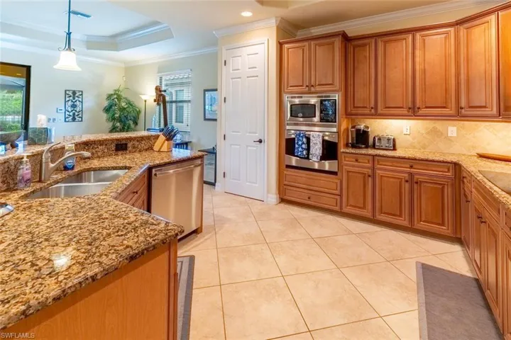 Kitchen featuring stainless steel appliances, a sink, brown cabinets, crown molding, and light stone countertops