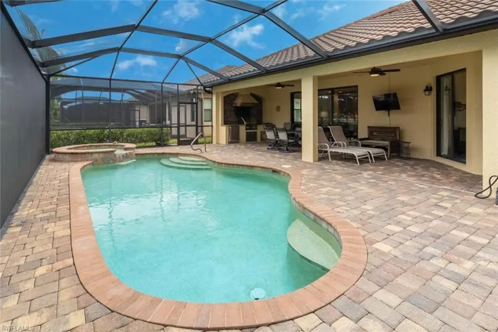 View of pool with glass enclosure, a ceiling fan, a pool with connected hot tub, and a patio