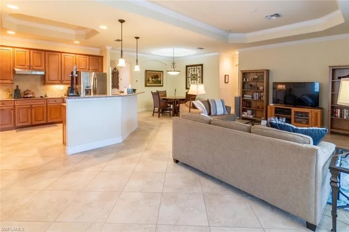 Living area with a raised ceiling, visible vents, ornamental molding, and light tile patterned floors