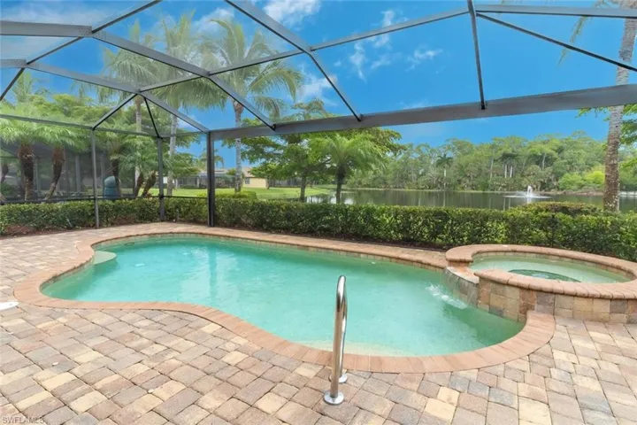 View of pool with a patio, glass enclosure, a pool with connected hot tub, and a water view