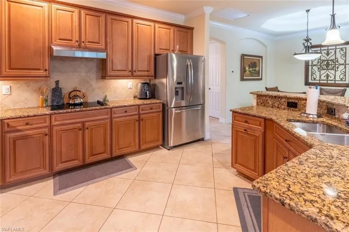 Kitchen featuring crown molding, brown cabinetry, stainless steel fridge with ice dispenser, black electric stovetop, and under cabinet range hood