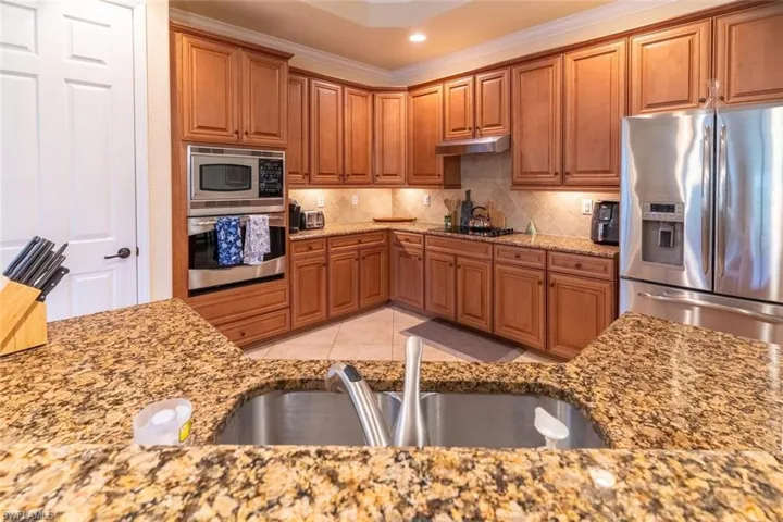 Kitchen featuring light stone counters, under cabinet range hood, stainless steel appliances, and a sink
