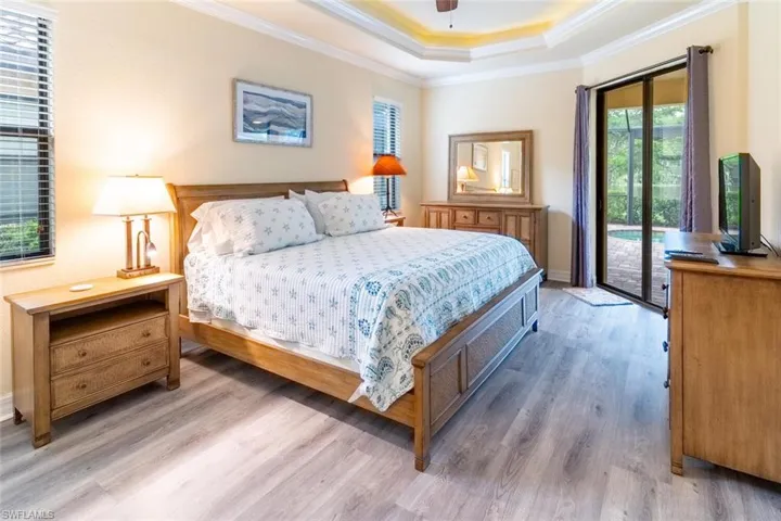 Bedroom with crown molding, wood finished floors, a tray ceiling, baseboards, and access to outside
