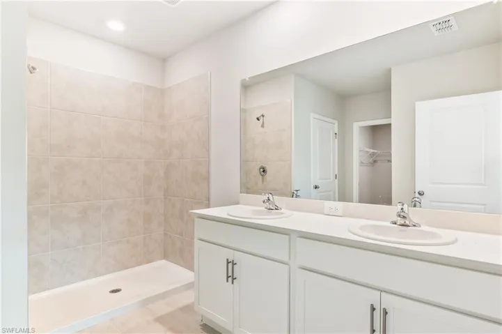 Bathroom with double vanity, a tile shower, and a spacious closet