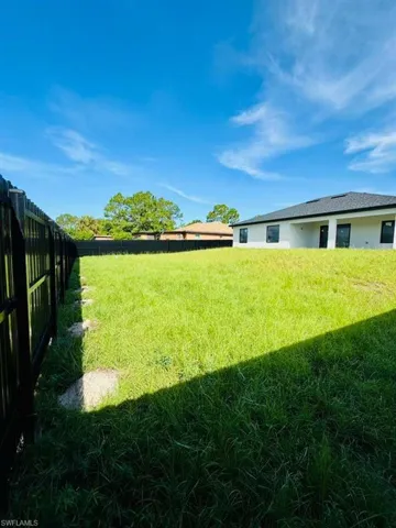 Expansive green space featuring a privacy fence, a new construction home, and a blue sky