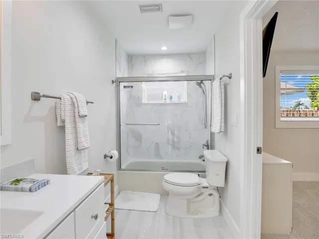 Full bathroom with bath / shower combo with glass door, toilet, and vanity