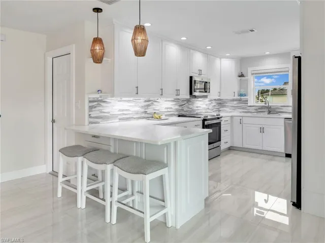 Kitchen featuring a kitchen bar, stainless steel appliances, white cabinets, kitchen peninsula, and decorative light fixtures