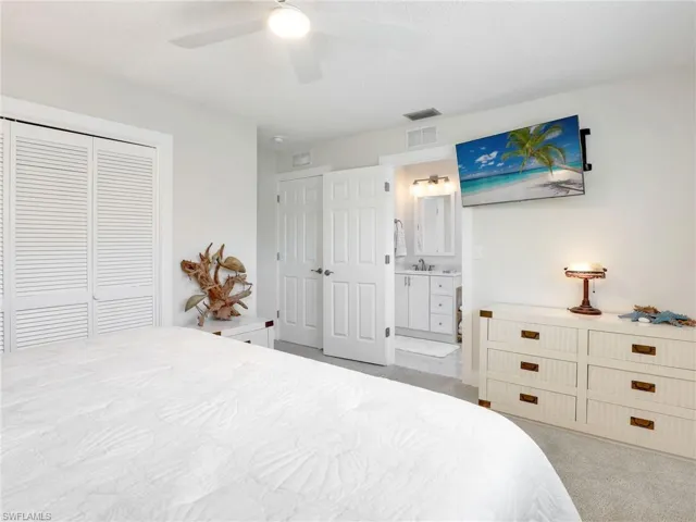 Bedroom with ensuite bathroom, ceiling fan, light carpet, and a closet