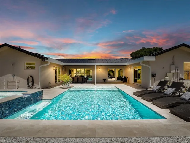 Pool at dusk with an in ground hot tub, a patio, and pool water feature