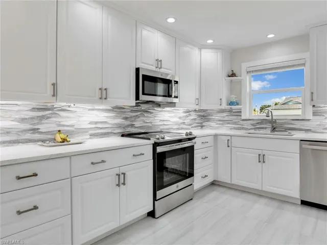 Kitchen with appliances with stainless steel finishes, backsplash, white cabinetry, and sink