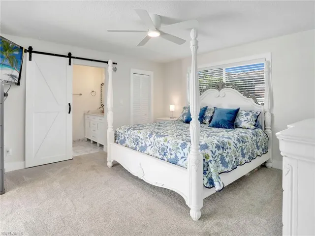 Carpeted bedroom featuring a closet, ensuite bath, a barn door, and ceiling fan