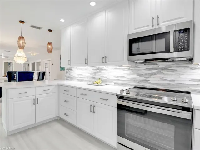 Kitchen with decorative light fixtures, tasteful backsplash, stainless steel appliances, white cabinets, and kitchen peninsula