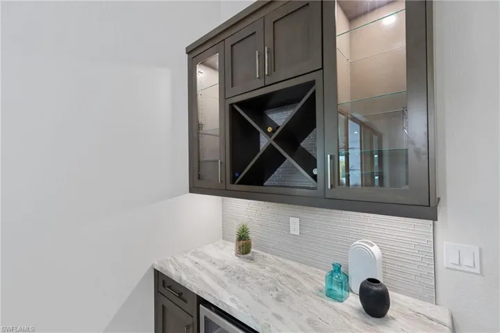 Bar with light stone counters, backsplash, and dark brown cabinetry