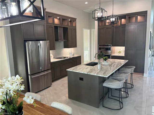 Kitchen with appliances with stainless steel finishes, backsplash, wall chimney exhaust hood, sink, and a center island with sink