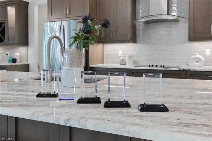 Kitchen with backsplash, light stone countertops, dark brown cabinets, wall chimney range hood, and black electric cooktop
