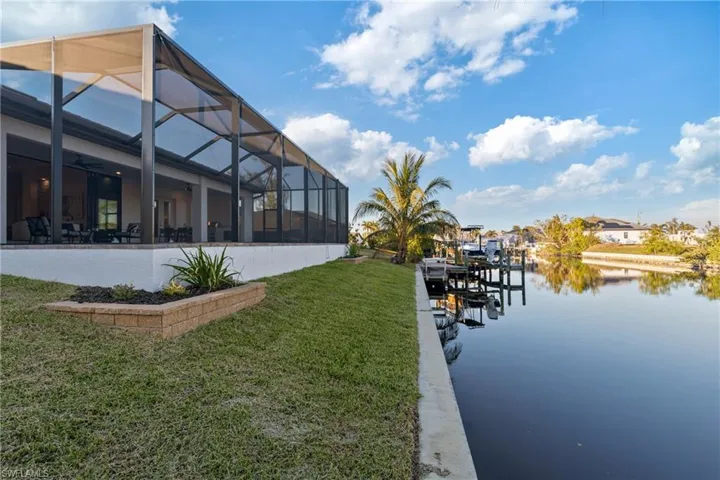 View of dock with a yard, a water view, and glass enclosure