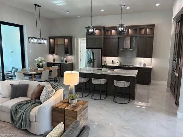 Kitchen featuring light stone countertops, wall chimney exhaust hood, pendant lighting, a center island with sink, and appliances with stainless steel finishes
