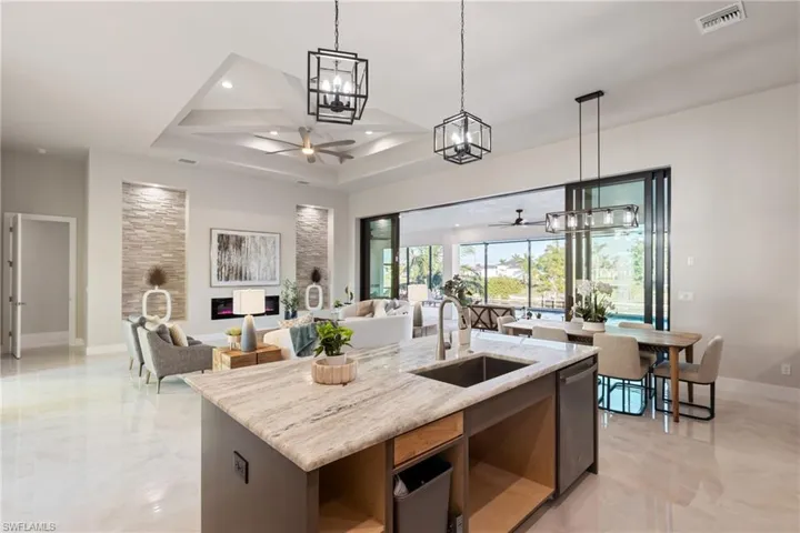 Kitchen featuring a kitchen island with sink, sink, stainless steel dishwasher, ceiling fan, and light stone counters