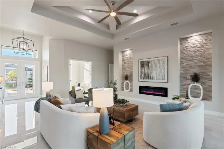 Living room with ceiling fan with notable chandelier, french doors, a high ceiling, and a tray ceiling