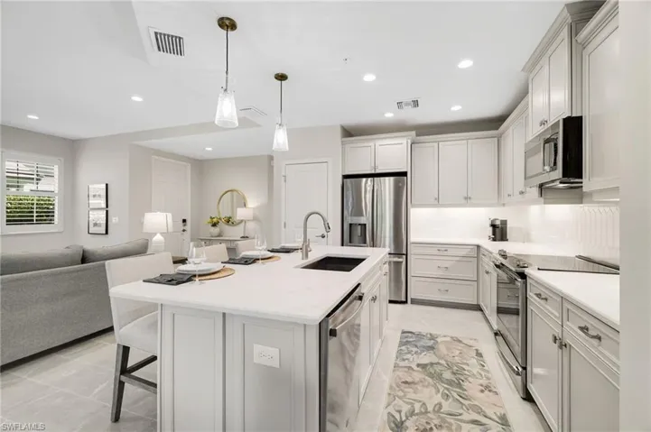 Kitchen featuring stainless steel appliances, a breakfast bar area, open floor plan, decorative light fixtures, and light stone countertops