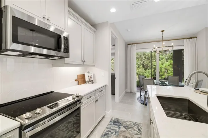 Kitchen featuring appliances with stainless steel finishes, light stone countertops, white cabinetry, recessed lighting, and a chandelier