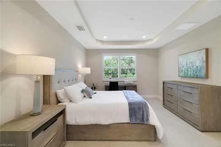 Bedroom with a raised ceiling, light carpet, and recessed lighting